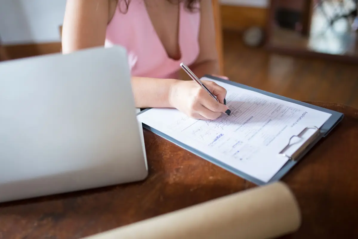 Een persoon maakt aantekeningen op een document naast een laptop