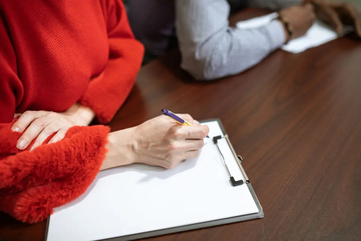 Handen die met een pen aantekeningen maken op een klembord